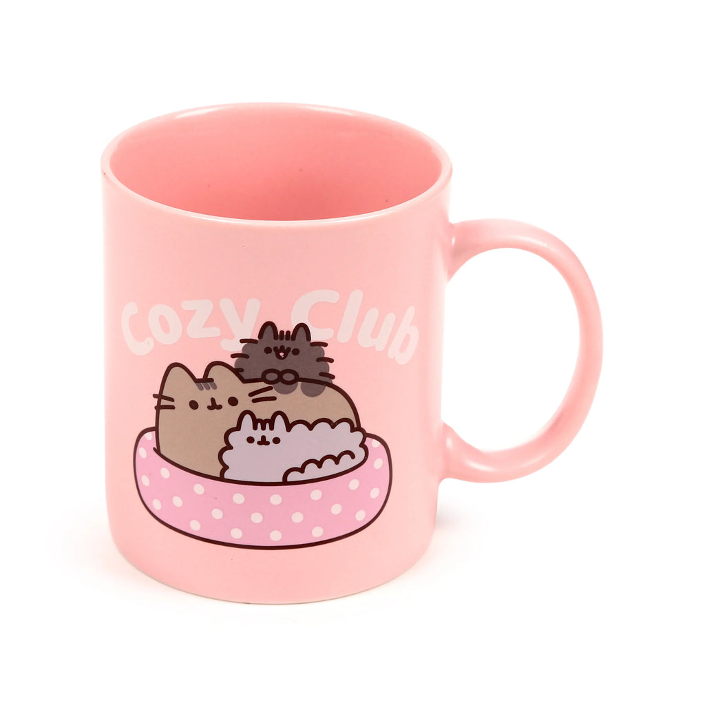 Front view of a pink porcelain mug displaying the Pusheen the Cat Cozy Club design, featuring Pusheen and two other cats snuggled in a pink polka-dot bed.