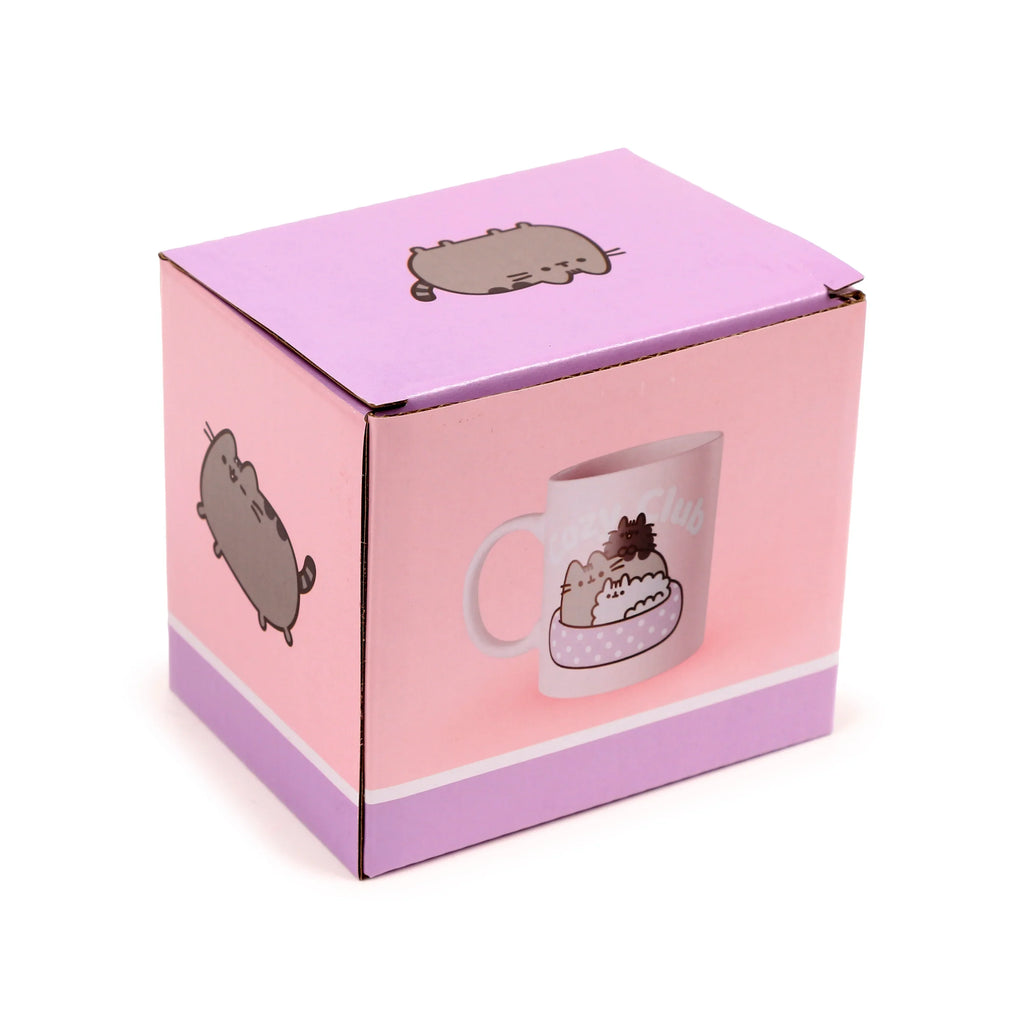 Angled view of a pink and purple cardboard box for the Porcelain Mug - Pusheen the Cat Cozy Club. The box features illustrations of Pusheen the Cat, including one depicting the mug design with Pusheen and kittens, and another of Pusheen lying down.