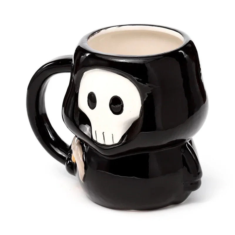 Angled view of a black novelty ceramic mug, shaped as a hooded figure with a white skull face, a cream-coloured interior, and a partially visible scythe detail.