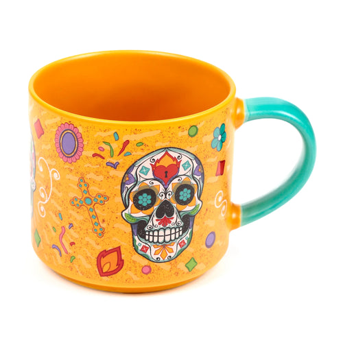 Angled view of a large yellow porcelain mug with a turquoise handle, featuring a vibrant multicoloured Day of the Dead sugar skull design and festive patterns.