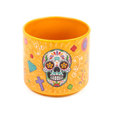 Angled view of an orange porcelain mug, decorated with a vibrant Day of the Dead sugar skull and colourful patterns including diamonds, crosses, and swirls.