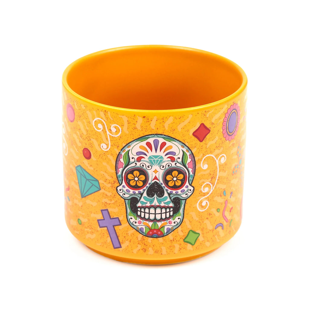 Angled view of an orange porcelain mug, decorated with a vibrant Day of the Dead sugar skull and colourful patterns including diamonds, crosses, and swirls.