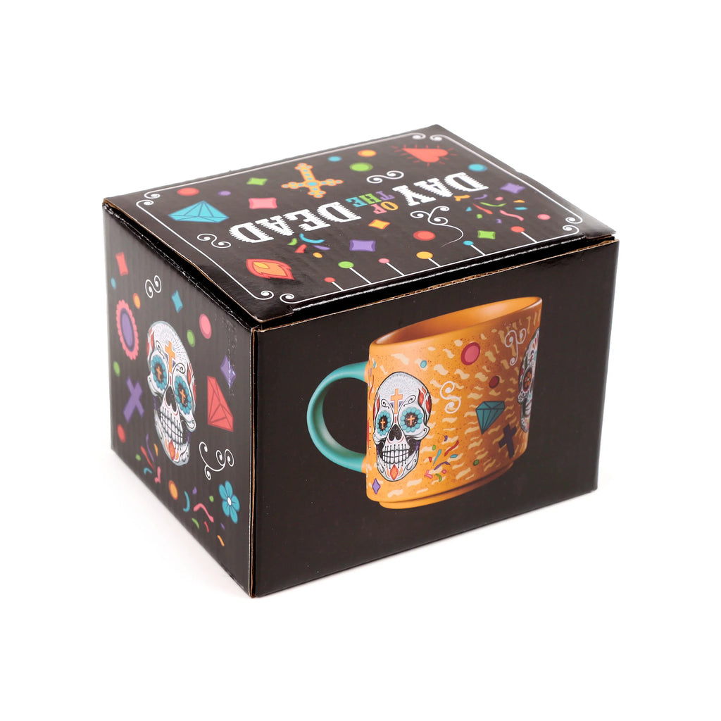 Angled view of the black gift packaging for a large Day of the Dead porcelain mug. The box features colourful sugar skull graphics and text, with one side displaying an image of the orange mug with a turquoise handle and white skull design.