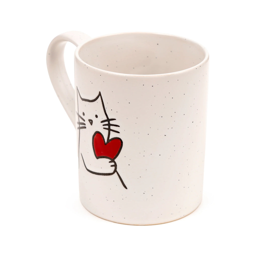 Angled view of a cream speckled stoneware mug, depicting a black outline drawing of a cat holding a red heart. The handle is visible on the left.