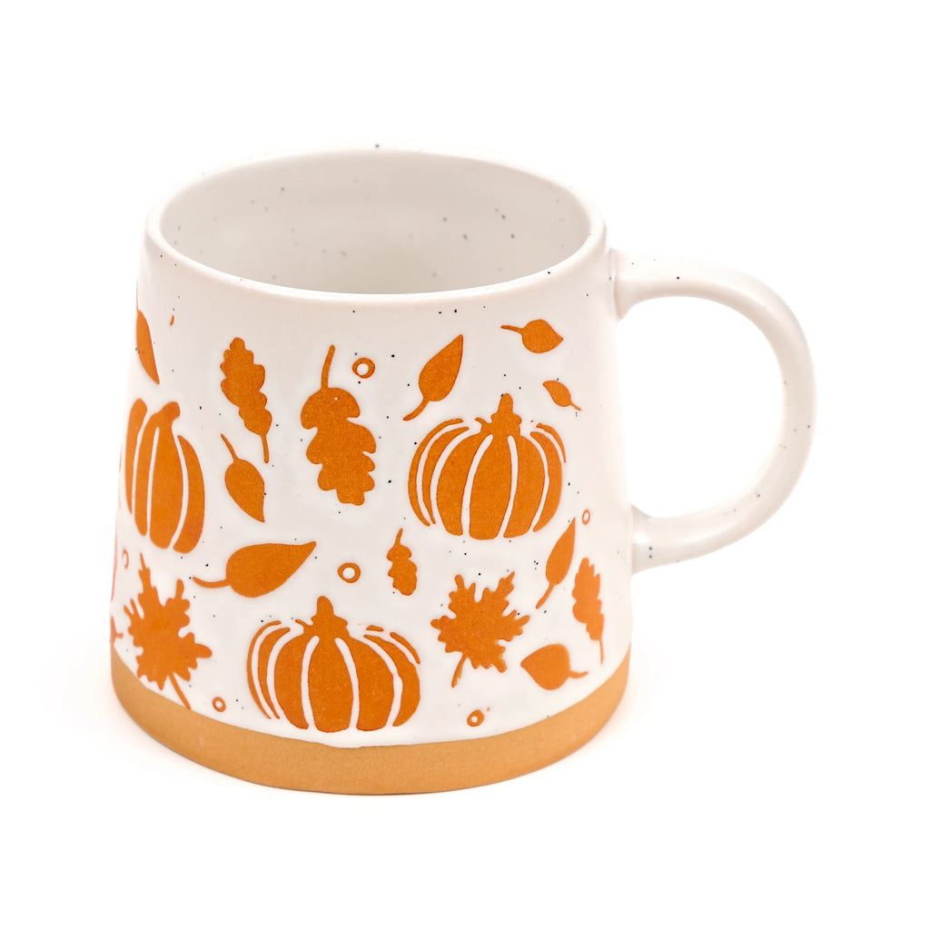 Angled view of a speckled cream stoneware mug, decorated with embossed orange pumpkin and autumn leaf motifs, with a natural unglazed stoneware base.