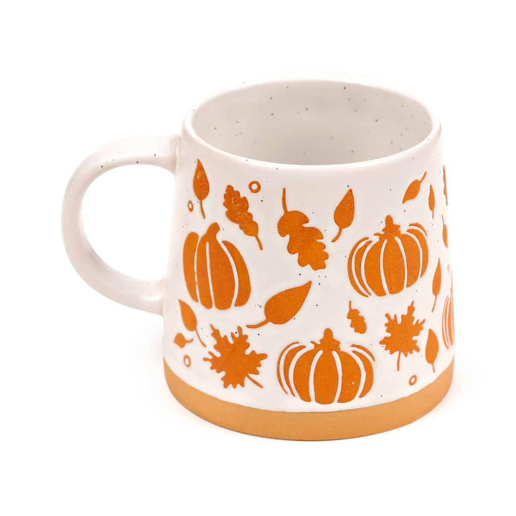 White speckled stoneware pumpkin mug, angled to show its orange autumn leaf and pumpkin pattern, with a visible handle and unglazed brown base.