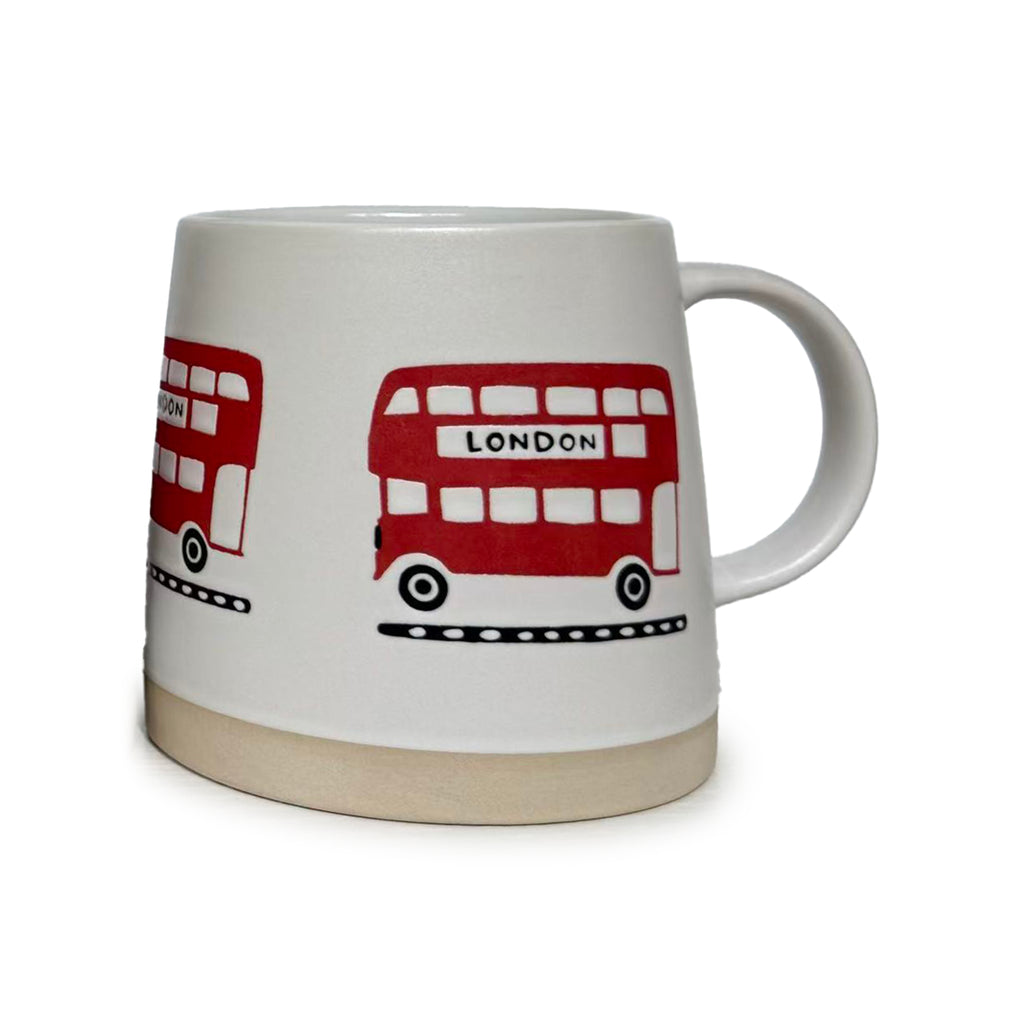 Angled view of a white tapered stoneware mug, featuring multiple red London bus illustrations with 'LONDON' text, a beige unglazed base, and a handle on the right.