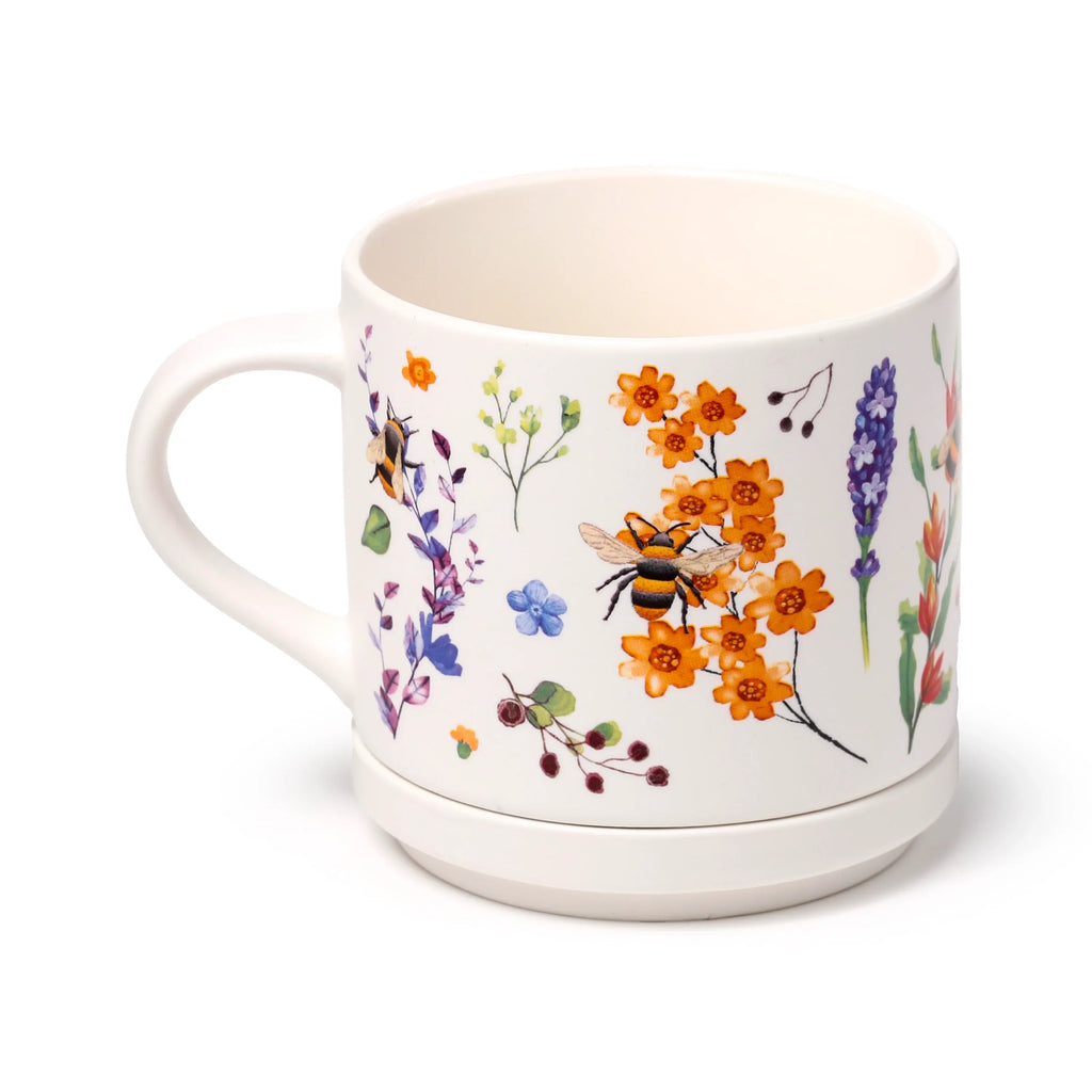 Angled view of a cream porcelain mug and matching coaster, decorated with colourful floral patterns including orange, purple, and blue flowers, green foliage, and bumblebees.