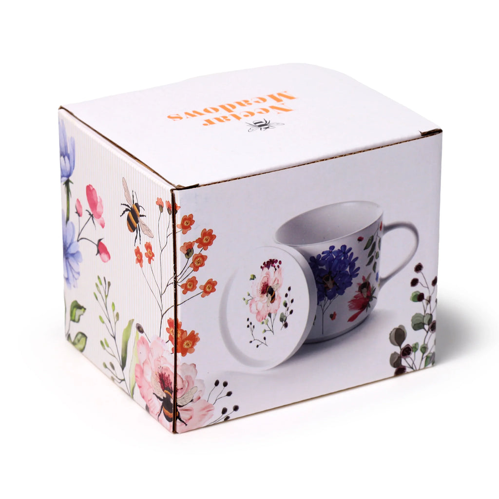 Angled view of a white cardboard product box, featuring an image of a porcelain mug and coaster lid set. The box is decorated with colourful floral patterns and bees, with the image on the box displaying a white mug with blue, red, and green floral designs, and a white coaster lid adorned with a pink flower and a bee.