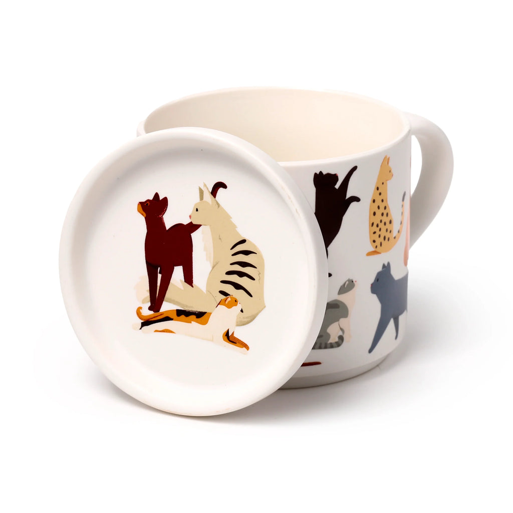 Angled view of a white porcelain mug and coaster lid set. The coaster, decorated with illustrations of brown, striped, and calico cats, leans against the mug, which features black, spotted, and grey cat designs.