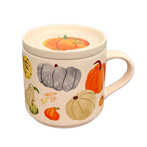 Angled view of a cream porcelain mug and matching coaster lid, featuring an autumnal design of various coloured pumpkins, gourds, and mushrooms. The mug's handle is visible on the right, and the lid is adorned with a large orange pumpkin.