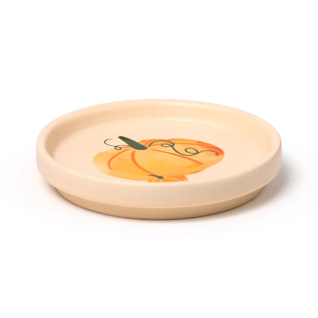 Angled view of a cream porcelain coaster lid featuring an orange pumpkin and green vine design.