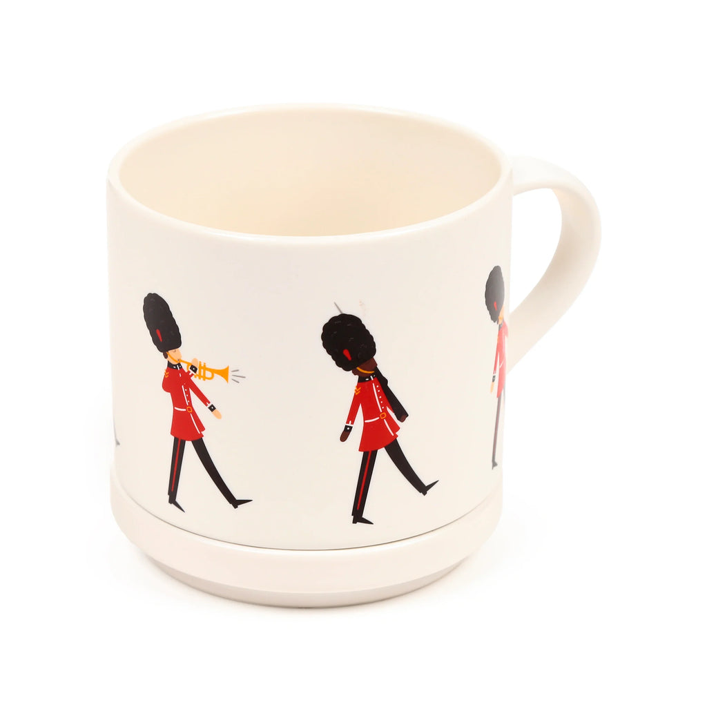 Angled view of a cream porcelain mug depicting a band of marching London Guardsmen in red tunics and black bearskin hats, with a handle on the right.