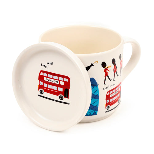 Angled view of a cream porcelain mug and coaster lid set, decorated with colourful London landmark illustrations, including red double-decker buses, guards, and 'beep! beep!' text.