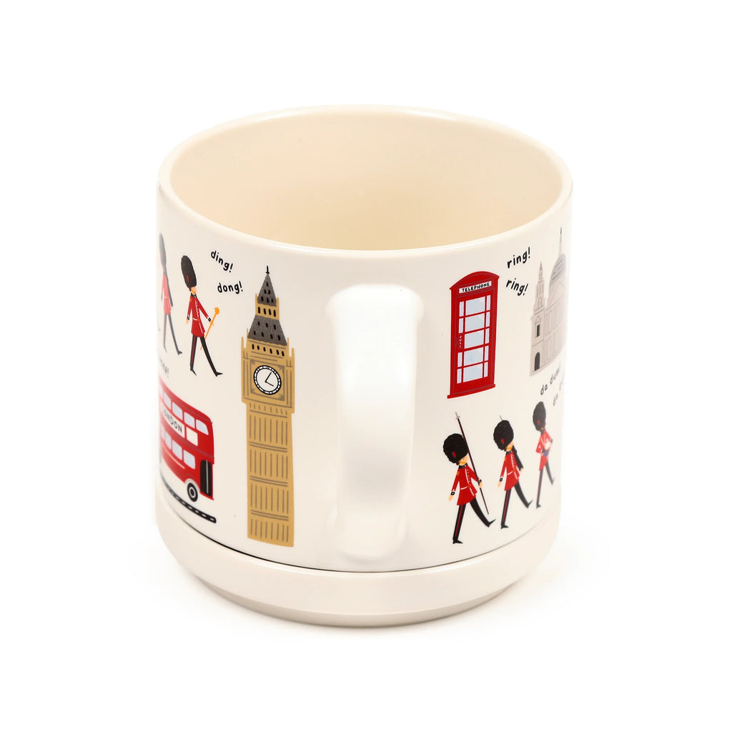 Angled view of an off-white porcelain mug and its coaster lid, featuring illustrations of London landmarks like a red double-decker bus, Big Ben, red telephone box, St Paul's Cathedral, and marching Queen's Guards.