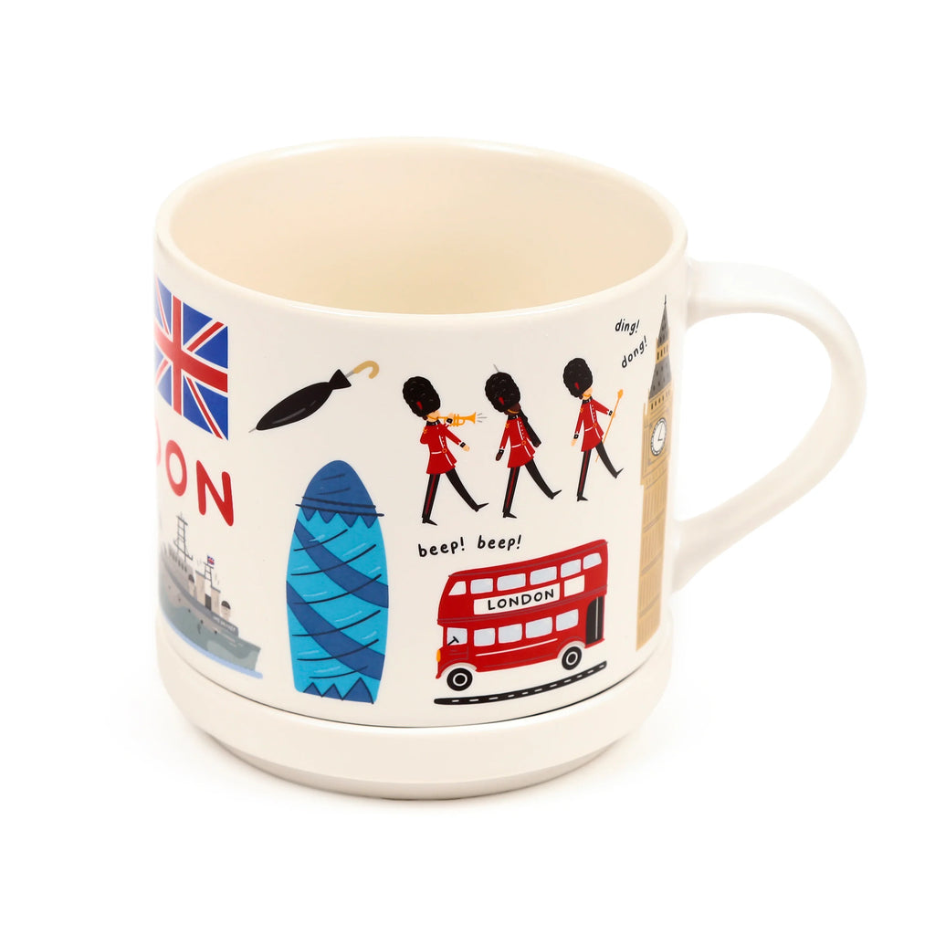 Angled view of a cream London souvenir mug featuring colourful cartoon illustrations of a double-decker bus, marching guards, Big Ben, the Gherkin, and a Union Jack flag. It has a wide, tiered base and a visible handle.