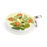 Angled view of a round manicure set case, featuring a tropical frog design with a green frog on a leaf against a light yellow background. The case has a white zip closure and a silver-coloured carabiner clip.