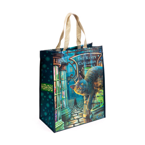 Angled view of a reusable shopping bag with a grey cat illustration on a cobbled street, featuring 'The Rusty Cauldron' shop, and dark blue side panels patterned with celestial symbols.