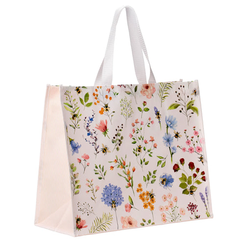 Angled view of a Durable Reusable Shopping Bag with a Nectar Meadows design, featuring a colourful floral and bee pattern on a white background. The tote has white fabric handles and a light, vertically striped side panel.