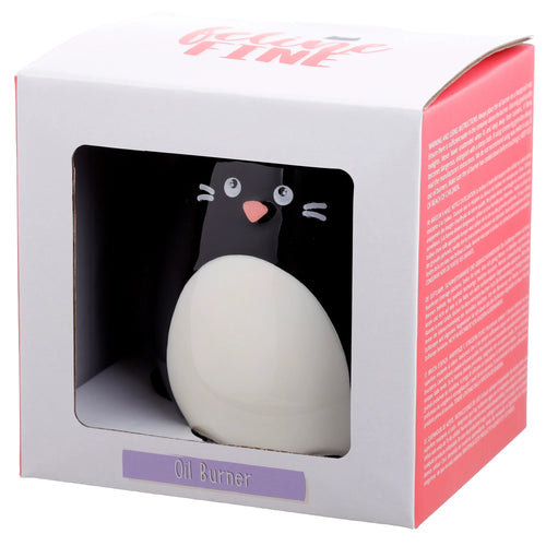 Angled view of a white product box with a window, showcasing a black and white ceramic cat-shaped oil burner. The cat features a pink nose, white eyes, and whiskers. The box displays 'Feline FINE' in pink lettering and a purple label with 'Oil Burner'.