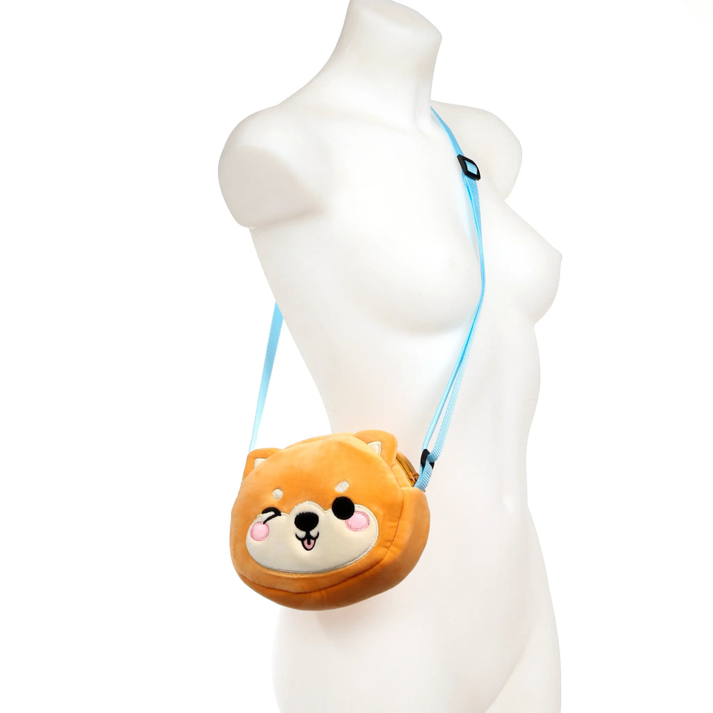 Front view of a plush brown Shiba Inu cross body bag with a winking face, white muzzle, and light blue strap, worn on a mannequin.