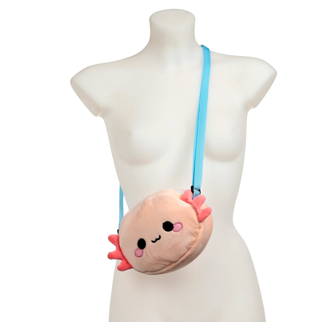 Front view of a plush peach axolotl crossbody bag with pink gills, embroidered black eyes, mouth, and pink cheeks, displayed on a white mannequin with a light blue strap.