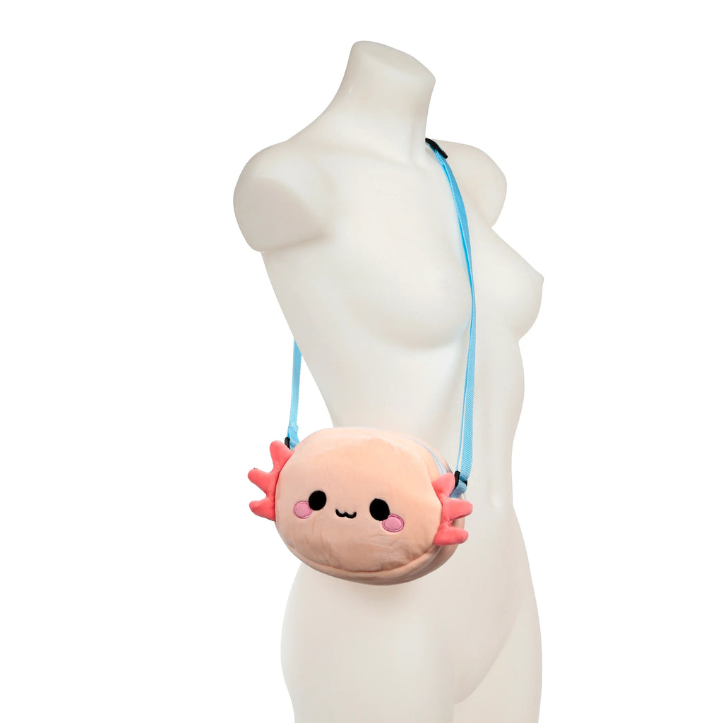 Front view of a plush axolotl crossbody bag, featuring a pale pink body with black embroidered eyes and mouth, pink embroidered cheeks and frilly gills, and a light blue adjustable strap, displayed on a white mannequin's torso.