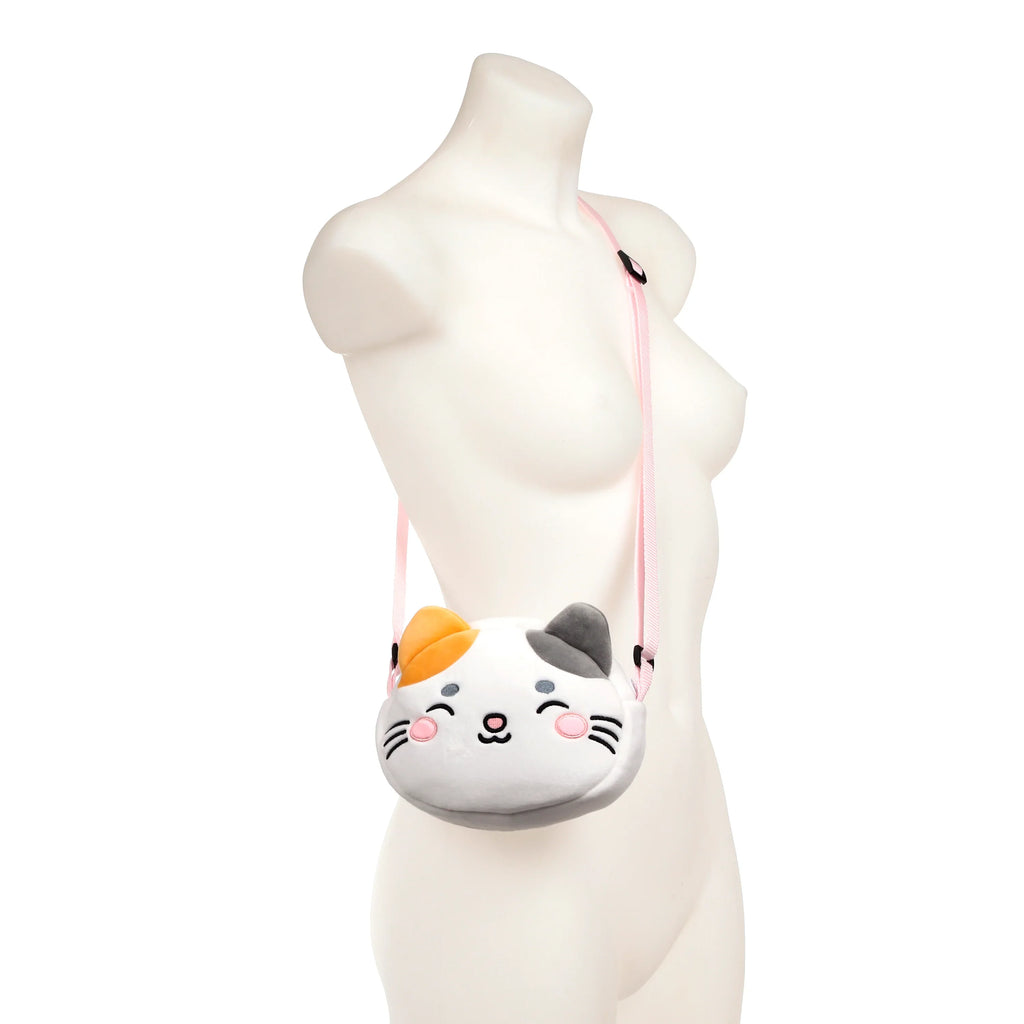 Front view of a plush white, orange, and grey cat face cross body bag, featuring embroidered eyes, nose, and whiskers, with a pink strap, displayed on a mannequin.
