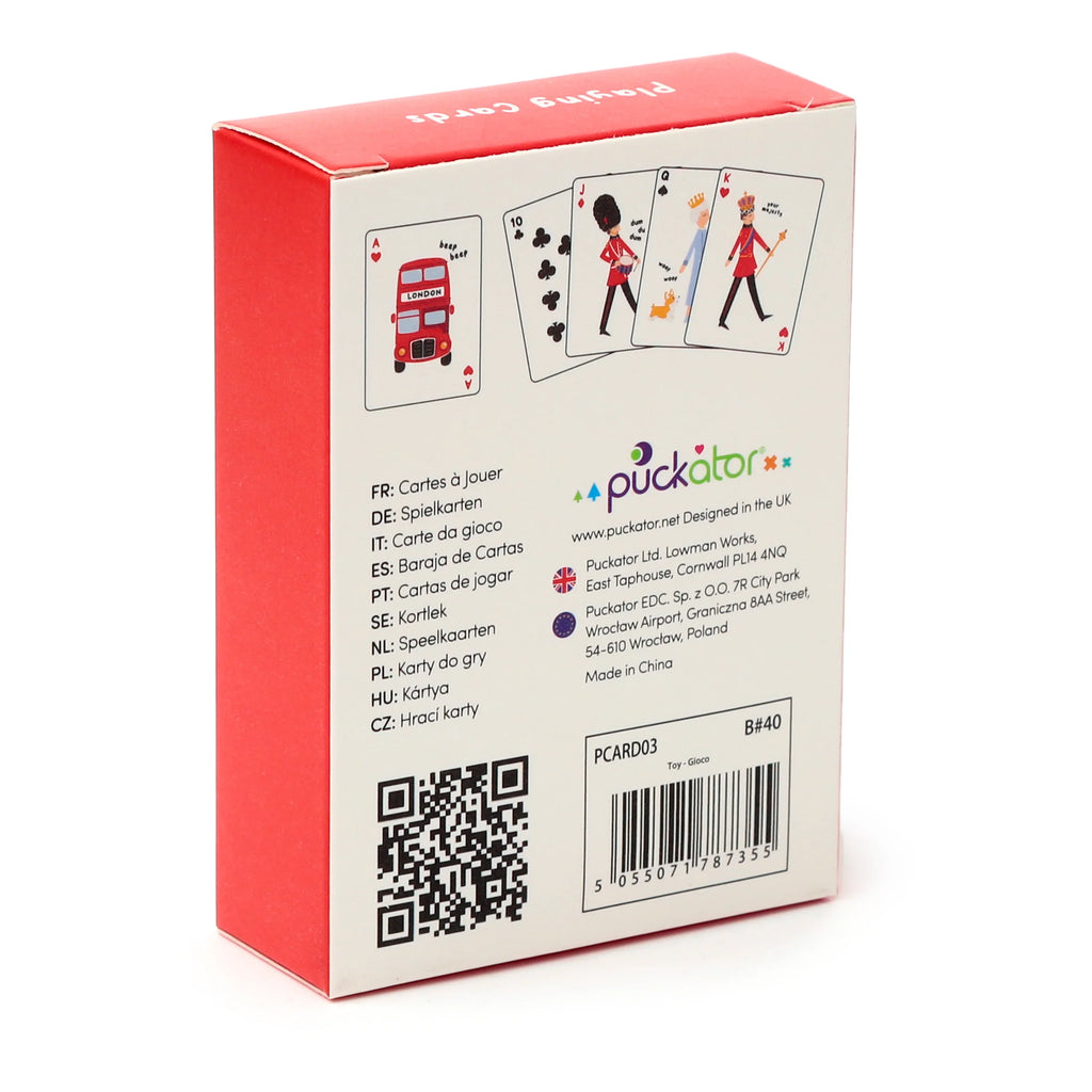 Angled view of the Standard Deck of Playing Cards London souvenir retail box. The white packaging features cartoon illustrations of playing card faces, including a red London double-decker bus, a Grenadier Guard, a corgi dog, and a royal figure. The box has a visible red side and top flap.