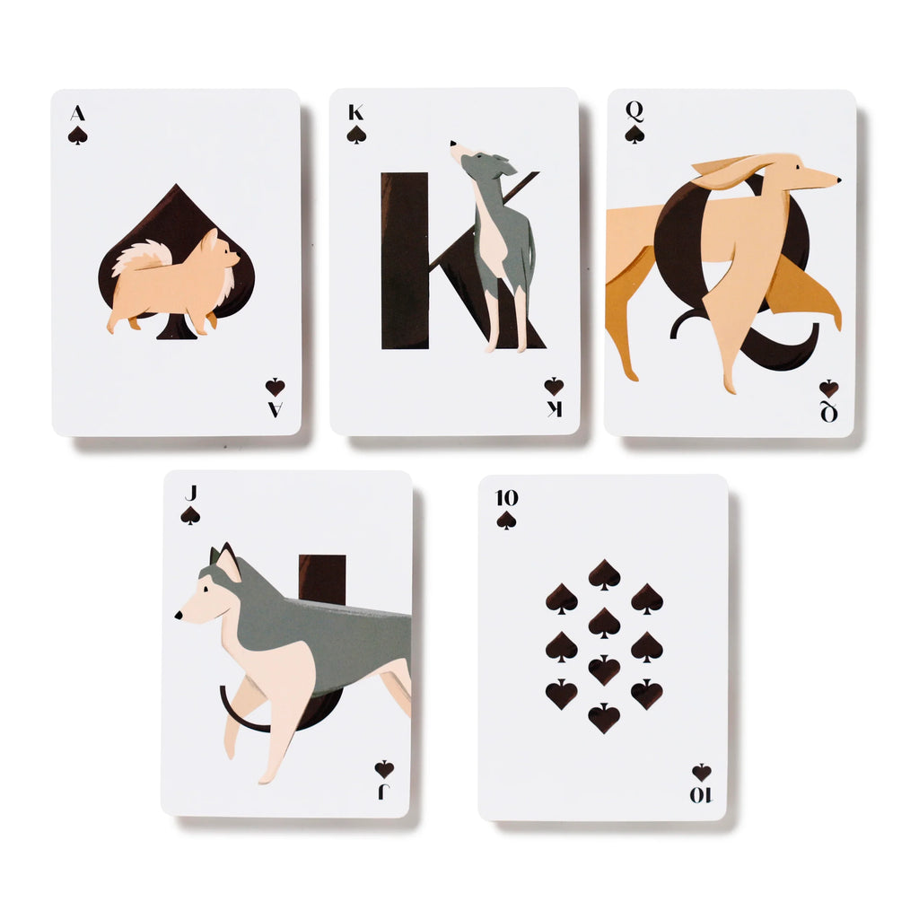 Overhead view of five white playing cards from the Spades suit: the Ace featuring a fluffy brown Pomeranian, the King with a greyhound, the Queen with a dachshund, the Jack with a husky, and the 10 of Spades, all displaying black spade symbols on a plain white background.