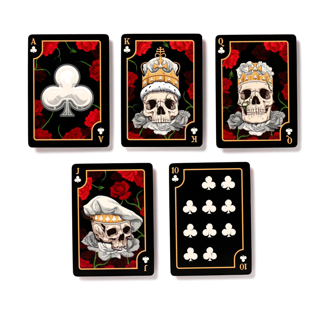 Flat lay of five black playing cards from a Skulls and Roses deck, featuring red roses and golden borders on a white background. The Ace, King, Queen, Jack, and Ten of Clubs are displayed. The King, Queen, and Jack cards depict unique skull designs: the King wears a gold crown, the Queen a gold crown with pearl details, and the Jack a white hat, all surrounded by white roses. The Ace card shows a large white club symbol, whilst the Ten card displays ten white club symbols.