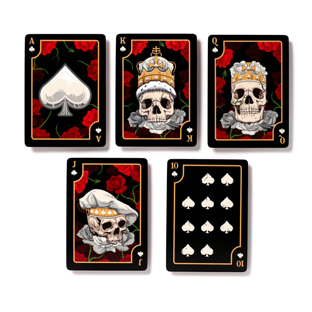 A top-down display of five 'Skulls and Roses' playing cards, including the Ace, King, Queen, Jack, and 10 of Spades. Each black-backed card features red roses; the King, Queen, and Jack depict skull designs wearing crowns or a chef's hat, while the Ace and 10 show prominent spade symbols. All cards are finished with decorative gold borders.
