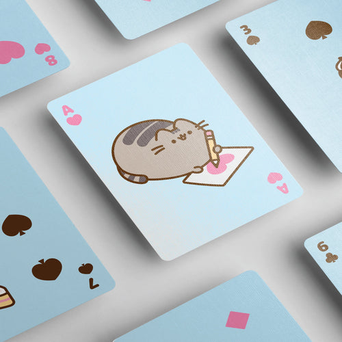 Angled close-up of several light blue Pusheen the Cat playing cards, featuring an Ace of Hearts with Pusheen drawing a pink heart. Other cards displaying various suits are partially visible.