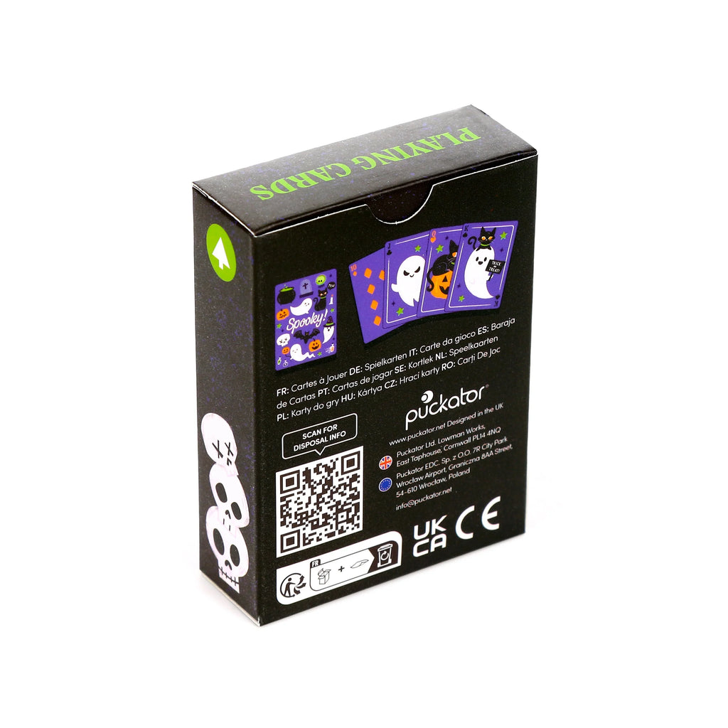 Angled view of a black Spooky playing cards deck box. The front panel displays Halloween-themed playing card designs featuring ghosts, pumpkins, and a black cat. The top panel has 'PLAYING CARDS' in green text, and the side panel shows stacked skull graphics. Multilingual text, a QR code, and UK/CE marks are also visible.