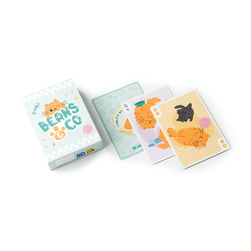 Angled view of a Standard Deck of Beans & Co Cats playing cards, featuring a light blue tuck box with a winking orange cat, and fanned-out cards depicting various cartoon cats, paw prints, and fish bones.