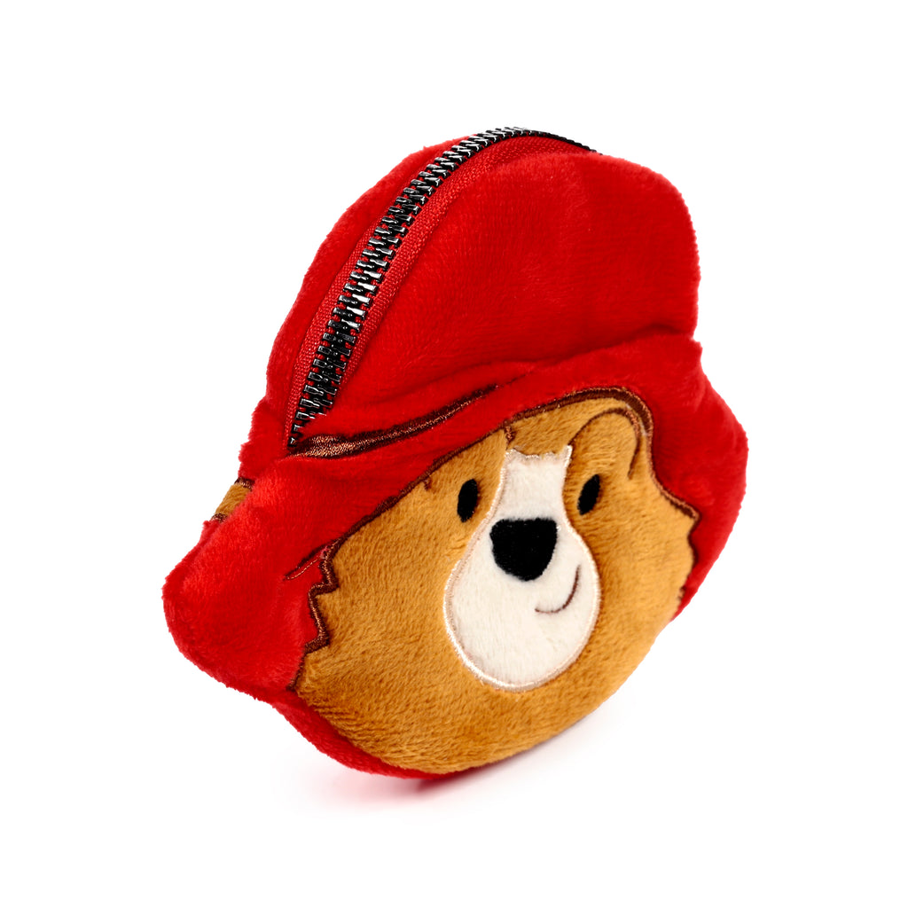 Angled view of a plush Paddington Bear change purse featuring a red hat, brown bear face, white snout, black nose, embroidered smile, and a black zipper along the top.