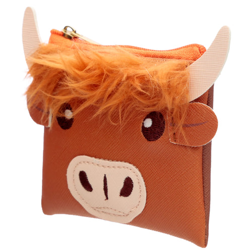 Angled view of a brown PVC Highland Coo cow purse, featuring an orange fluffy fringe, beige horns, embroidered eyes, a light-coloured snout, and an orange zip closure.