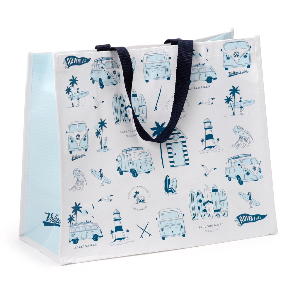 Angled view of a white recycled reusable shopping bag with navy blue webbing handles. The front and visible left side display a light blue and navy ocean-themed motif, featuring Volkswagen T1 camper vans, surfers, palm trees, lighthouses, waves, and text including 'ADVENTURE' and 'EXPLORE MORE BEACH LIFE'. The side panel has a light blue wavy pattern.