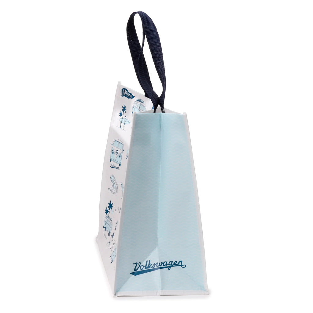 Angled view of a white recycled RPET reusable shopping tote bag featuring blue illustrations of a T1 camper bus, palm trees, and surfers. It has a light blue side panel with a wave pattern, dark blue handles, and Volkswagen script at the bottom.