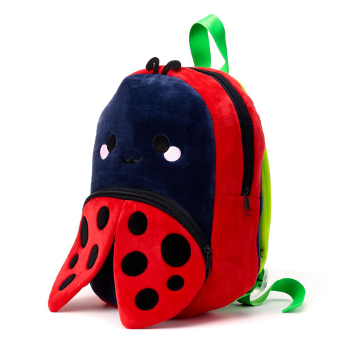 Front angle view of a plush red and blue ladybird kids school backpack with black spots, embroidered face, and green straps on a white background.