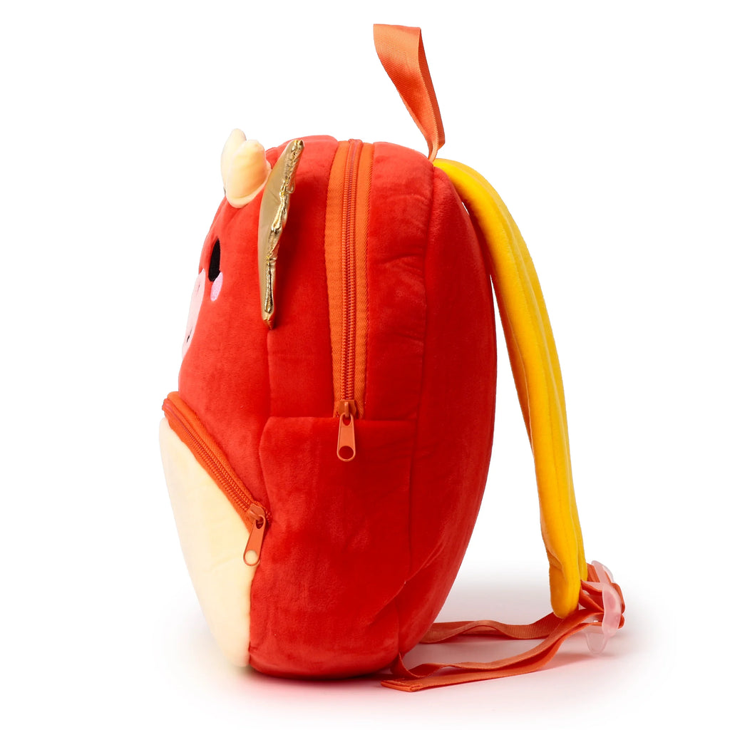 Side view of a red plush kids dragon backpack with yellow shoulder straps, gold horns, a top carry handle, and visible zippers.