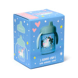 Angled view of a blue product box for a reusable, shatterproof sippy cup. The box displays the sippy cup with a white unicorn, pink hearts, and rainbow 'Unicorn Magic' design, alongside an illustration of its hygienic cover.
