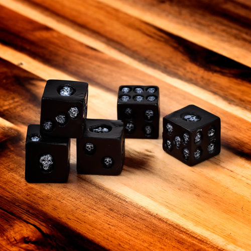 Angled view of five black cubic skull dice, showing their white carved skull designs on various faces, resting on a polished wooden surface.