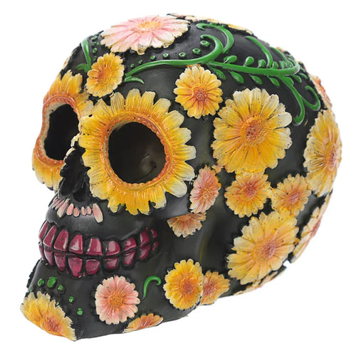 Three-quarter view of a black Day of the Dead skull ornament, intricately decorated with yellow and pink daisy flower patterns and green vines.