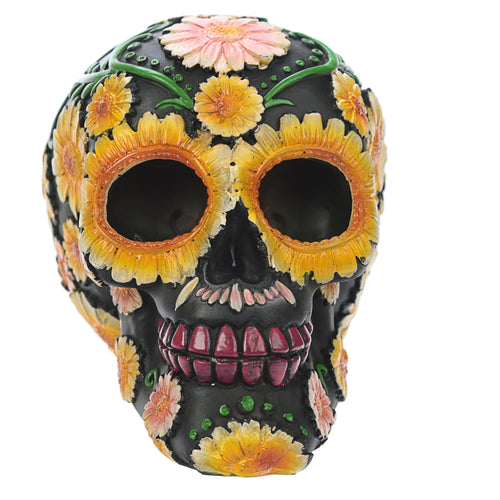 Front-angled view of a black Day of the Dead skull head ornament, adorned with yellow and pink daisy floral motifs, green vines, and red teeth.