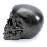 Angled profile of a metallic black skull decoration, highlighting its shimmering finish, detailed teeth, and crack details.