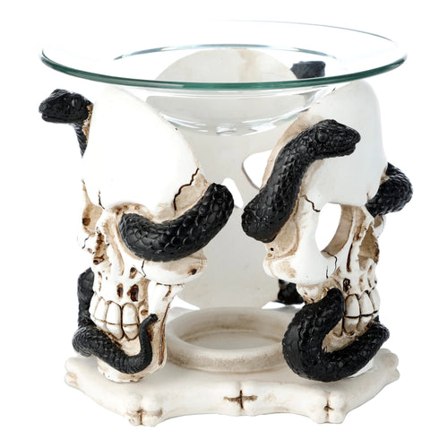 Angled view of an aged white resin skull and serpent oil and wax burner with a clear glass dish, showing the detailed skulls entwined with black serpents and an ornamental base.