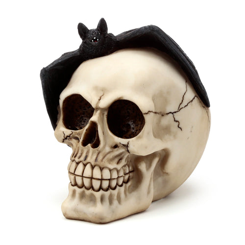 Angled view of a bone-coloured gothic skull decoration with dark eye sockets and detailed cracks, featuring a black bat ornament with spread wings perched on its head.