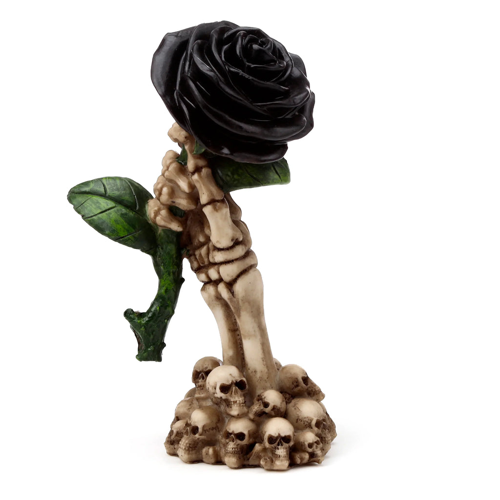 Front view of a gothic figurine depicting a black rose with green leaves held by a bone-coloured skeleton hand, resting on a pile of skulls.