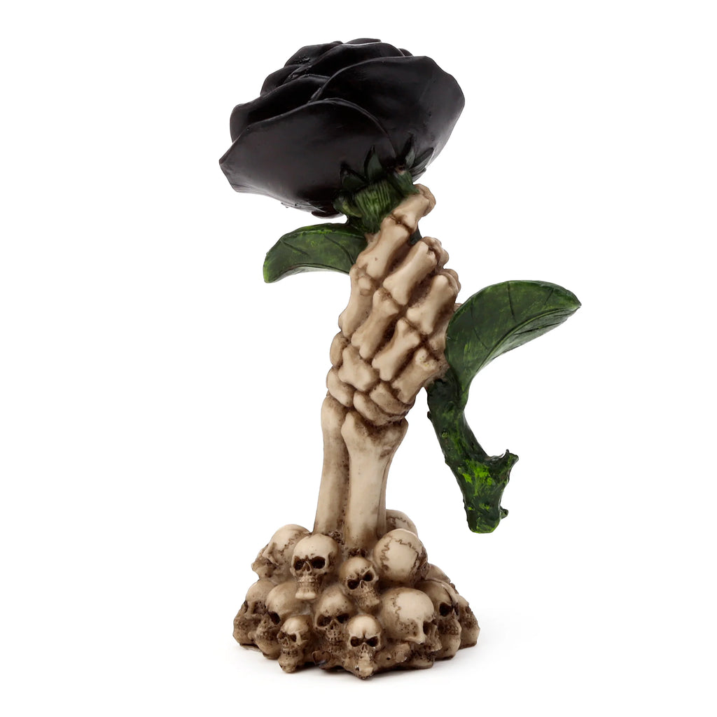 Gothic skull ornament featuring a bone-coloured skeleton hand clutching a black rose with dark green leaves, standing on a base of piled skulls.